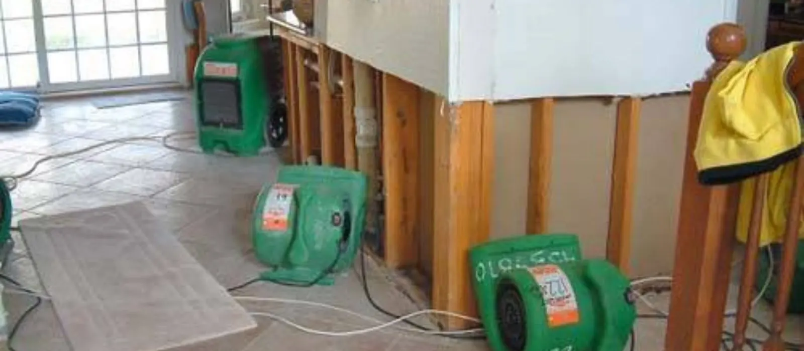 Green air movers set up to dry a wall cavity and floor